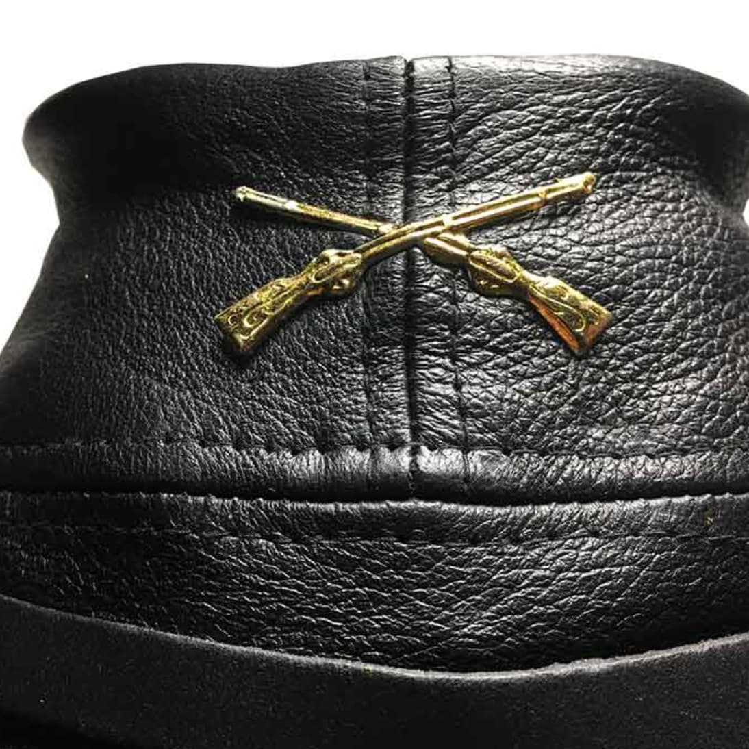 Primer plano del cordón dorado entrelazado y el emblema metálico en la gorra confederada de cuero negro.